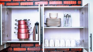 Un armario de cocina con ollas, una tetera y utensilios de cocina frente a una pared de ladrillo.