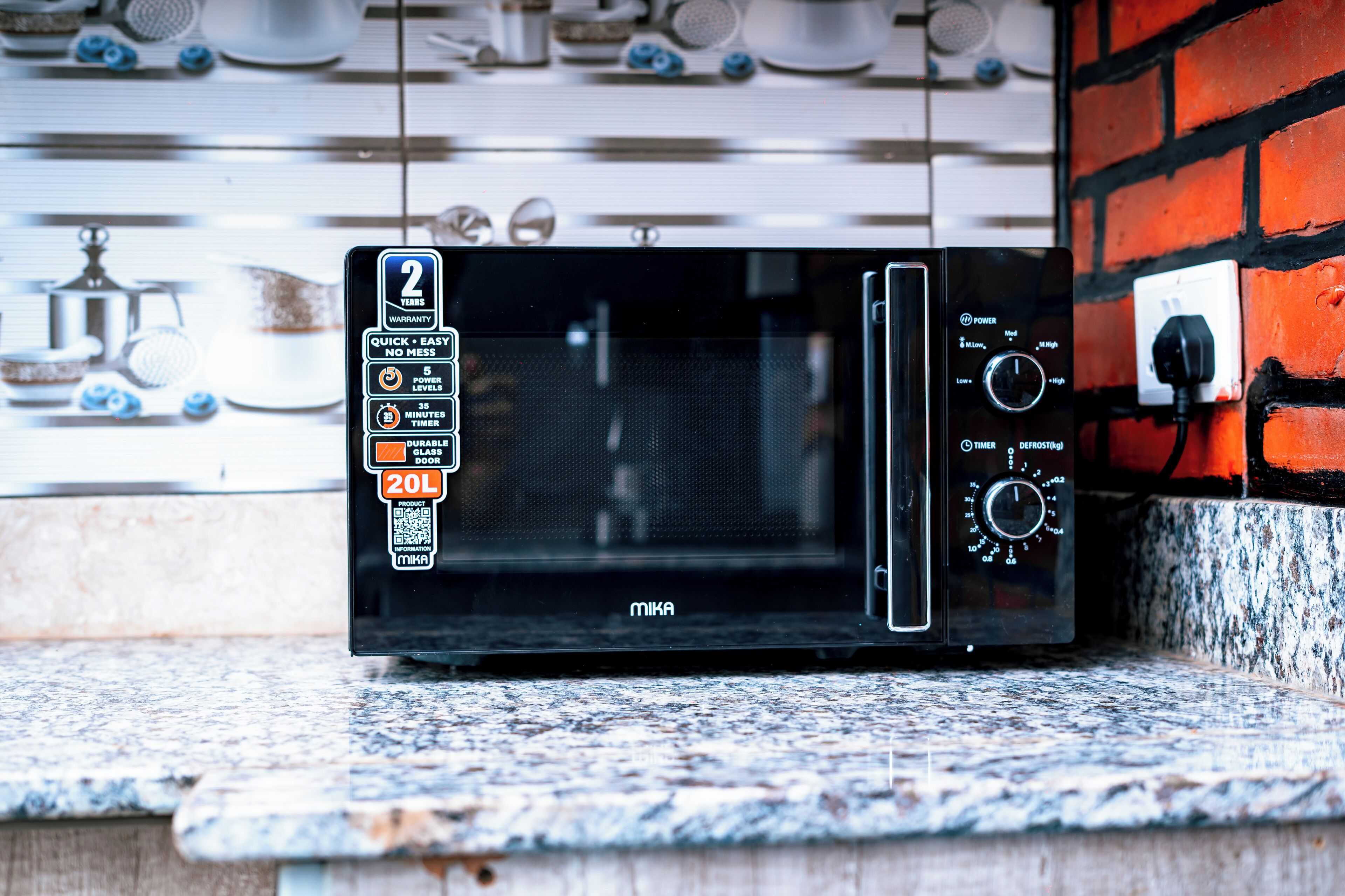 A black microwave oven on a granite countertop with a 2-year warranty sticker, a timer, and a power dial.
