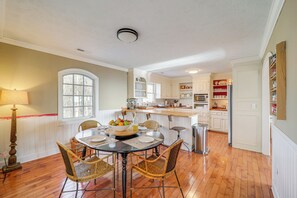 Une cuisine avec un plancher en bois, une table à manger avec des chaises, une fenêtre et des meubles de rangement blancs.