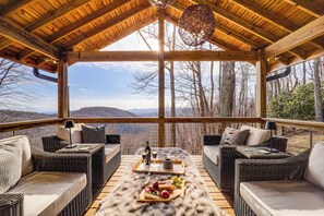 Un espace extérieur aménagé, abrité et doté de meubles en osier et d’une table à manger, offrant une vue sur un paysage montagneux.