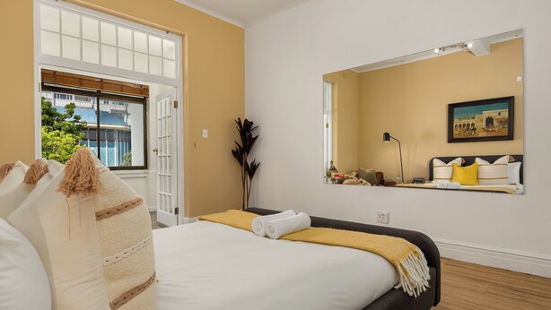 Une chambre à coucher avec un lit, une grande fenêtre, un miroir et un tableau accroché au mur.
