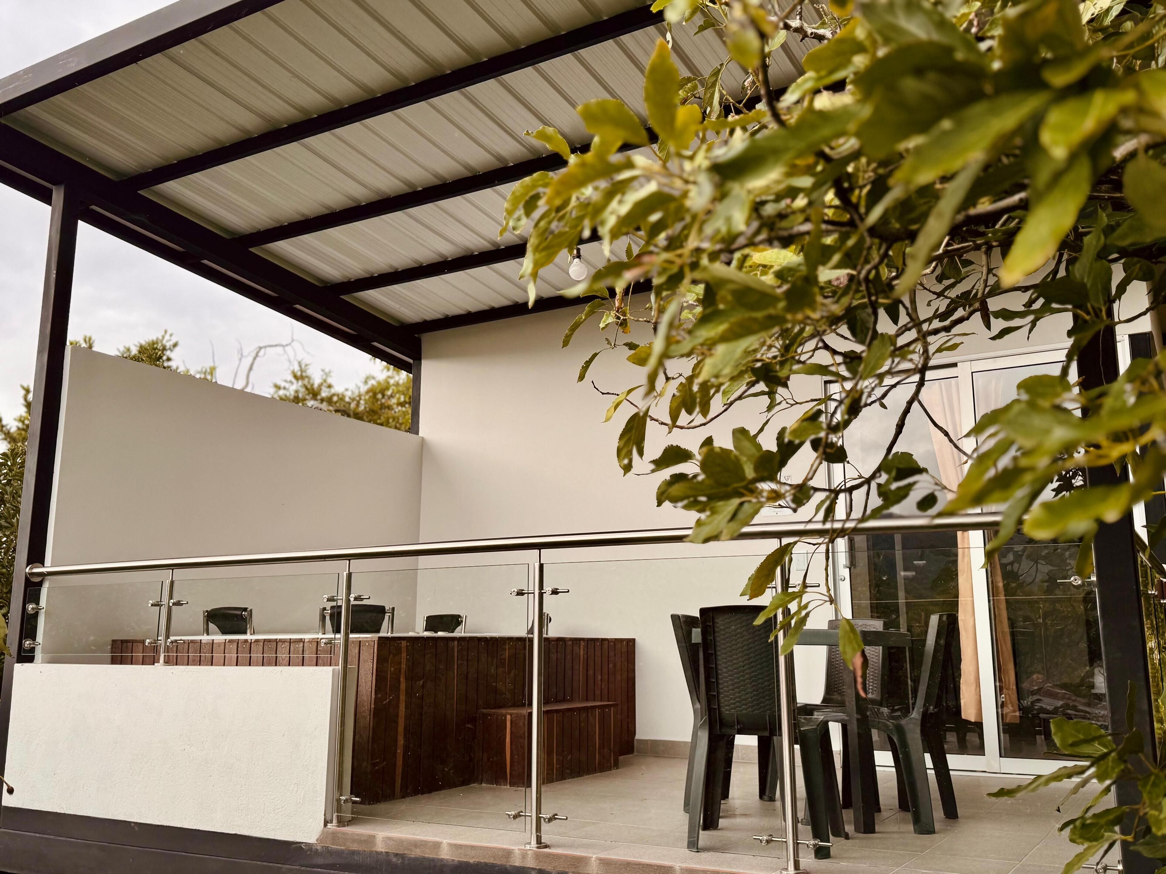 Un espace patio extérieur moderne, doté d’une balustrade en verre, de mobilier en bois et offrant une vue sur un bâtiment en arrière-plan.