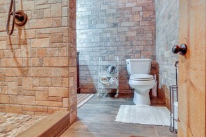 Un baño con pared de piedra, inodoro blanco, toallero de metal y puerta de madera.