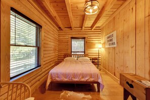 Un dormitorio tipo cabaña de troncos con cama, mesita de noche, silla y un cartel que dice 'SWEET HOME ALABAMA'.