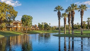 Un campo de golf con un estanque, palmeras y un edificio de varios pisos.