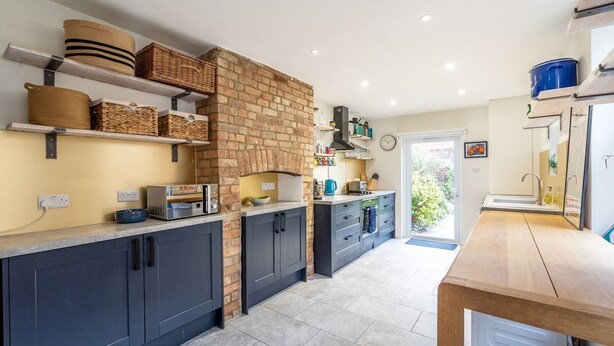 A modern kitchen with dark cabinets, a brick wall, and a wooden table.