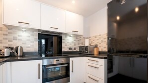 Una cocina moderna con armarios blancos, un refrigerador negro y electrodomésticos de acero inoxidable.
