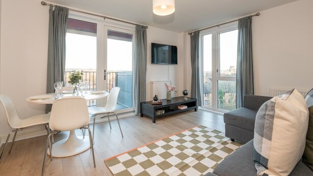 Una sala de estar moderna con comedor, ventanas grandes, un televisor de pantalla plana y un tapete a cuadros.