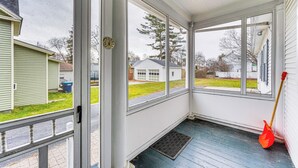 A covered porch with a view of a residential neighborhood, a red broom leaning against the wall, and a clock on the wall. - Ski, Hike & Fish: Modern Rutland Home (Rutland)