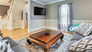 A living room with a wooden coffee table, grey sofa, and patterned cushions. A flat-screen TV is mounted on the wall. - Ski, Hike & Fish: Modern Rutland Home (Rutland)