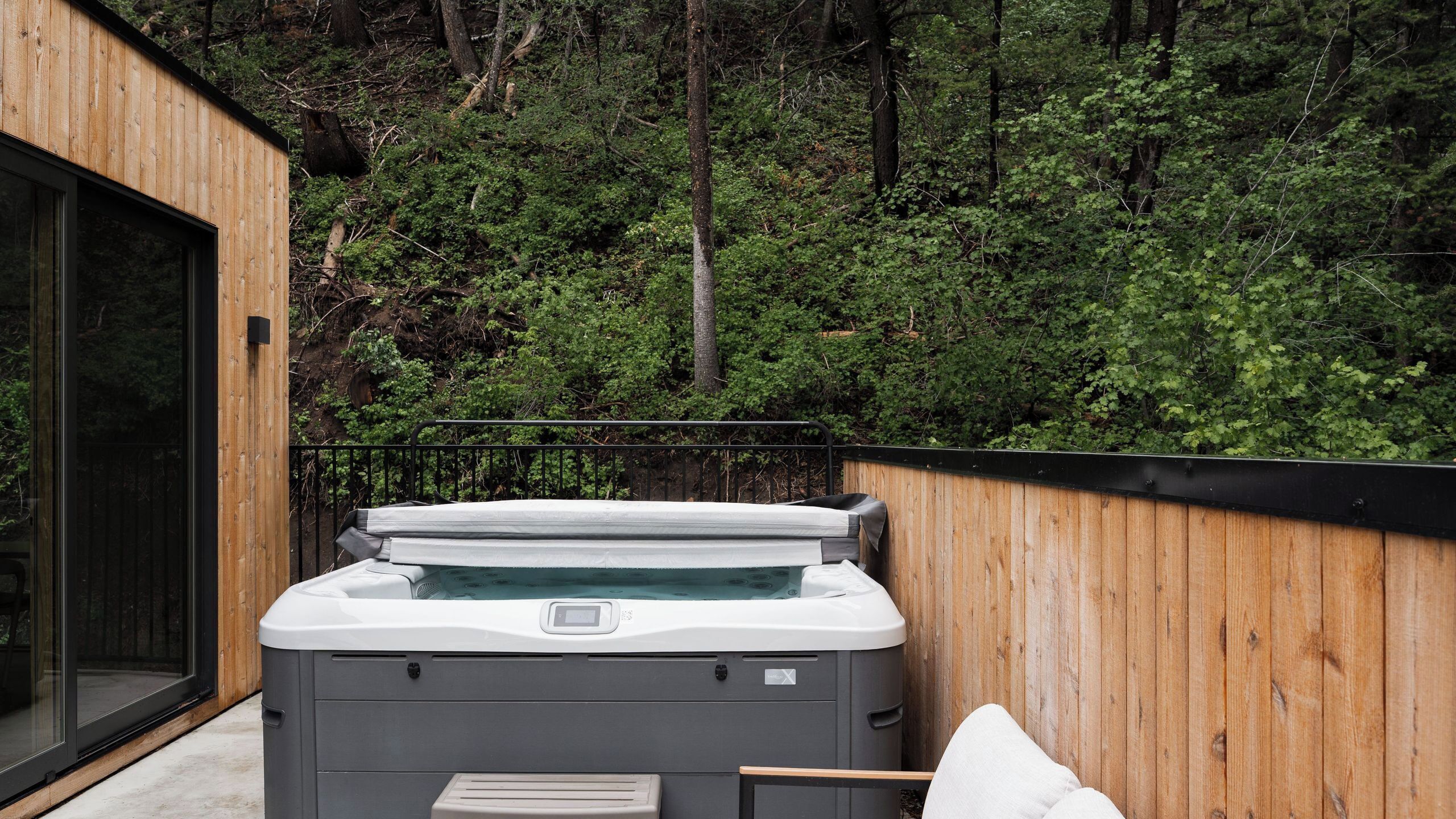 A hot tub in a wooden outdoor area with a view of a forested hillside.