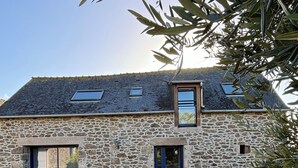 Ein Steinhaus mit Schotterauffahrt, einer kleinen Terrasse mit Stühlen und einer Tür mit Fenster darüber.