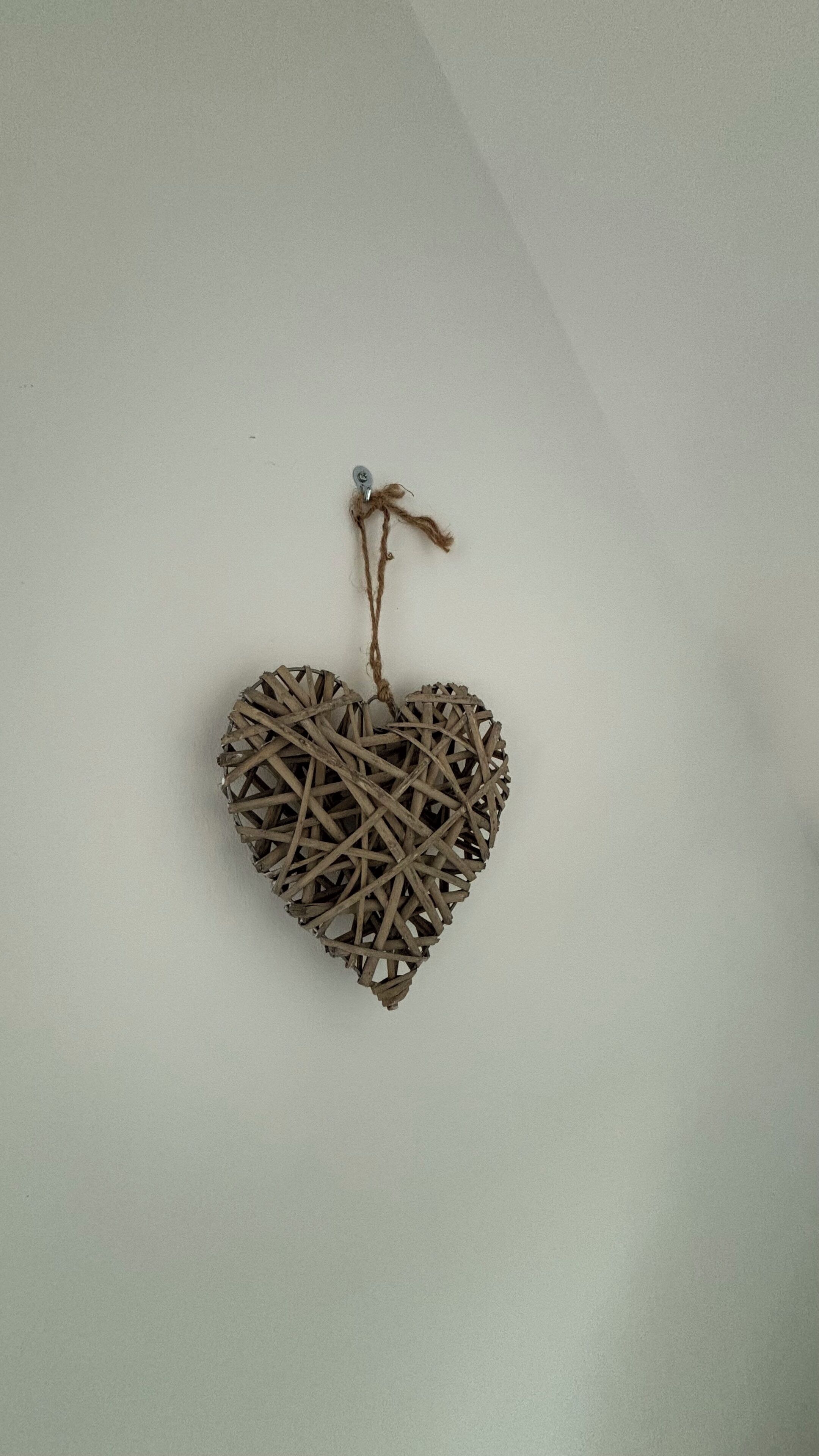 En hjerteformet dekoration af flettet stykker, hængende på en ensfarvet væg.