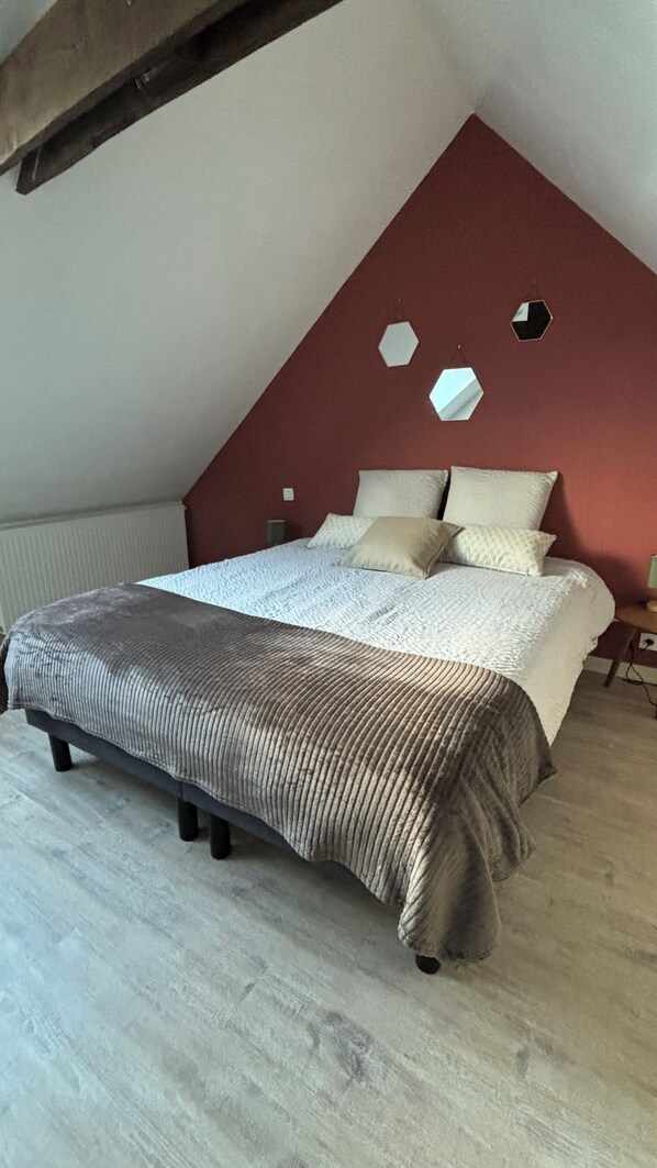 Un dormitorio con techo inclinado, una cama con colcha a rayas y una pared de acento roja.