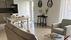 Ein modernes Wohnzimmer mit einem beigefarbenen Sofa, einem gestreiften Sessel und einem Couchtisch. Es gibt einen Essbereich mit Tisch und Stühlen, und im Hintergrund eine Küche.