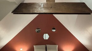 Ein Schlafzimmer mit schrägen Wänden, einem Bett mit Kopfteil, zwei Nachttischlampen und einem großen Fenster.