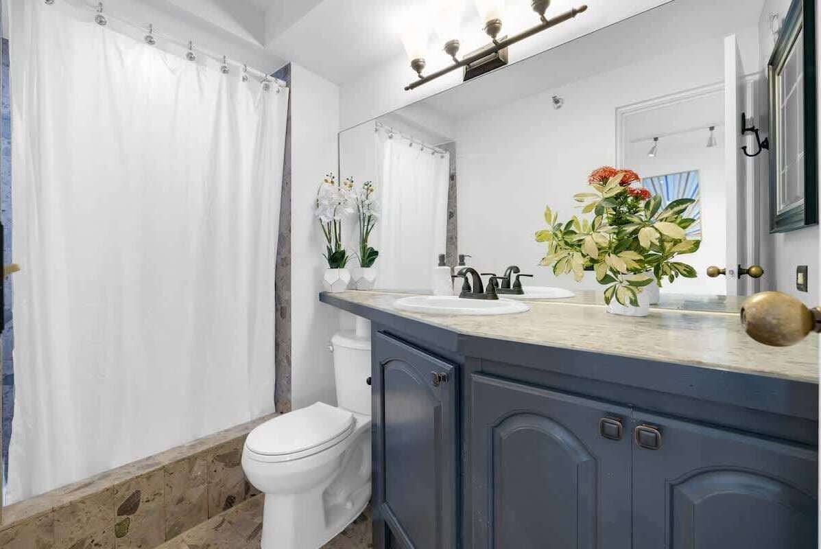 A bathroom with a white toilet, a shower curtain, a sink with a mirror above it, and two potted plants.