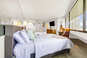 A hotel room with a large bed, a desk, and a chair. There is a TV on the wall and a window with a view of buildings. - Waikiki Forever Ocean Views, Free Parking & Pool (Honolulu)