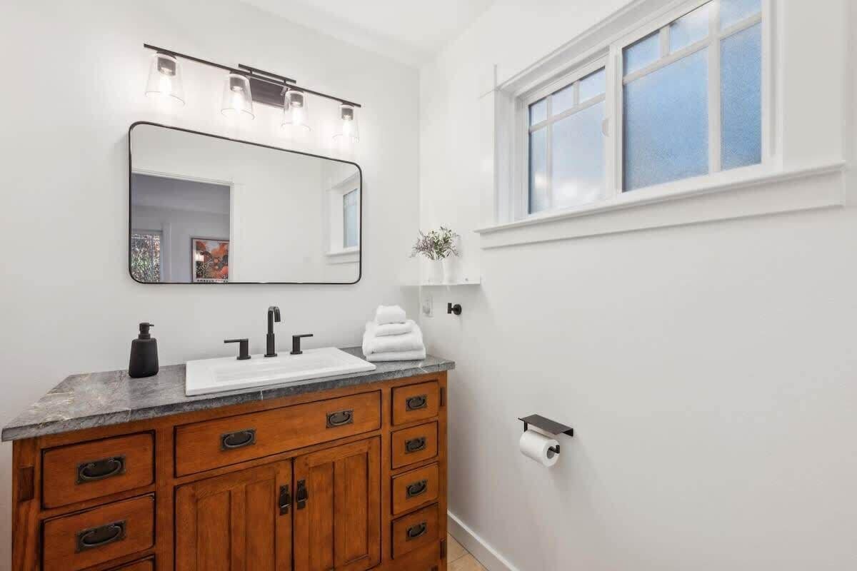 A bathroom with a wooden vanity, a large mirror, a white sink, and a window.