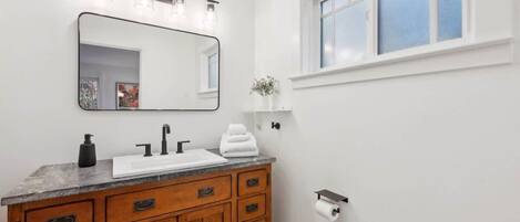 A bathroom with a wooden vanity, a large mirror, a white sink, and a window.