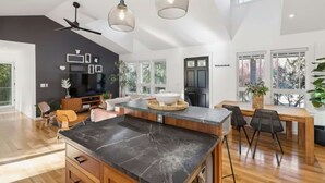 A spacious kitchen with a large island, modern pendant lights, and a dining area with a wooden table and chairs. - Ravenwood Paradise: Private Pool and Hot Tub (Glen Ellen)