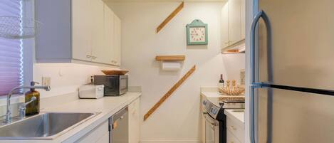 A kitchen with a sink, toaster, microwave, wooden shelf, and a clock on the wall.