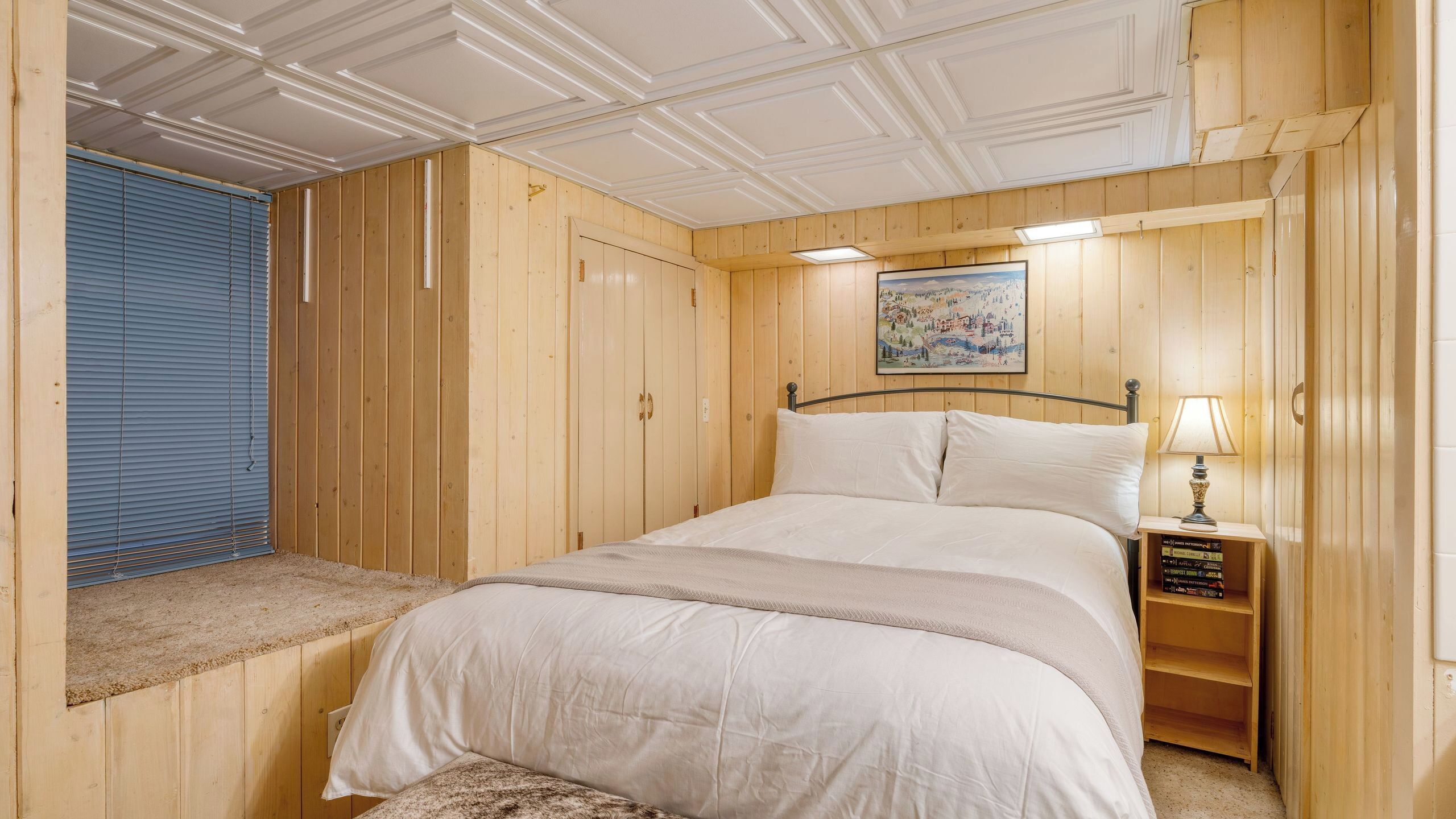 A wooden-paneled room with a bed, a nightstand, and a painting on the wall.