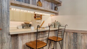 A kitchen with a wooden bar counter, two bar stools, a microwave, a toaster, and a clock on the wall. - Vail Vista Mountain Retreat w/ Balcony & Views, Near Vail Ski Village (Vail)