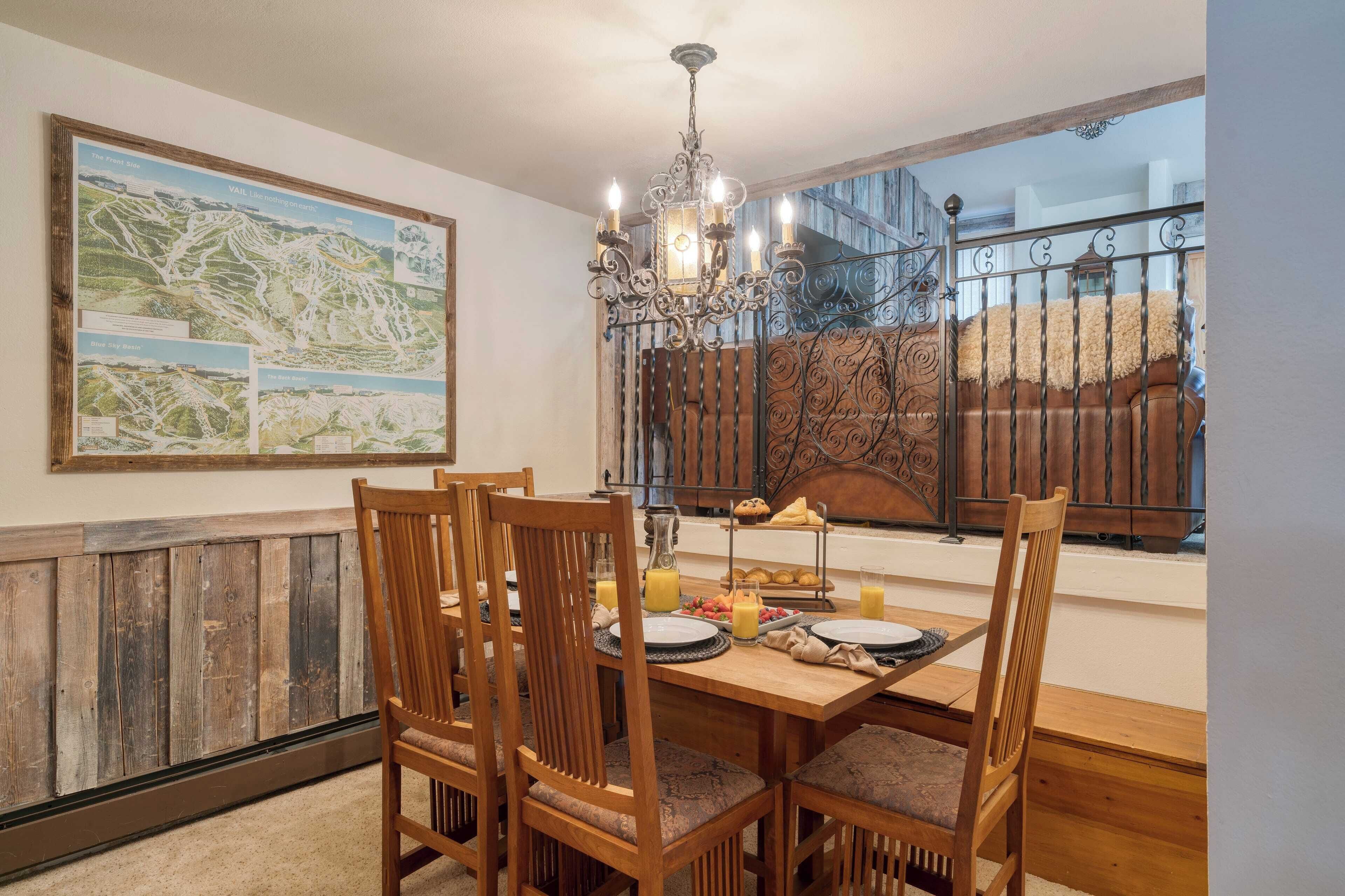 Un coin repas avec une table en bois, des chaises, un lustre et une carte accrochée au mur.