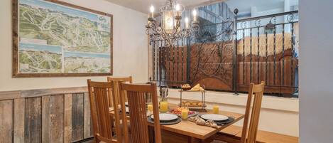 Un coin repas avec une table en bois, des chaises, un lustre et une carte accrochée au mur.
