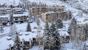 A snow-covered resort with multiple buildings, including a prominent multi-story structure with balconies, surrounded by snow-laden trees and hills. - Vail Vista Mountain Retreat w/ Balcony & Views, Near Vail Ski Village (Vail)