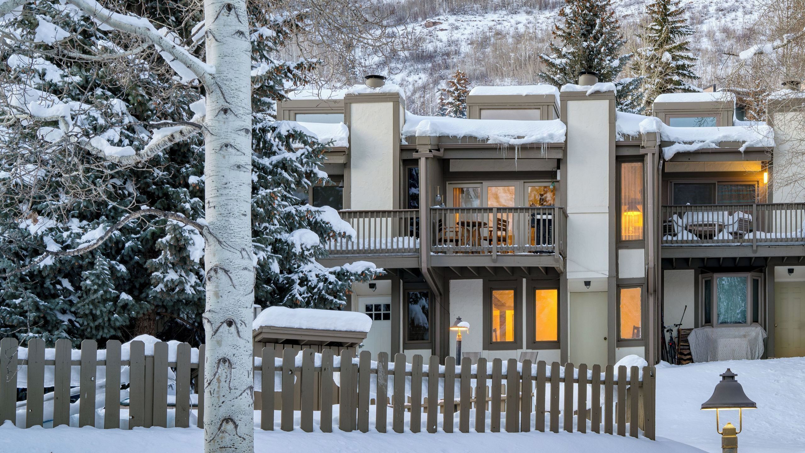 A multi-story building with a snow-covered exterior, a wooden fence, and a lit exterior light.