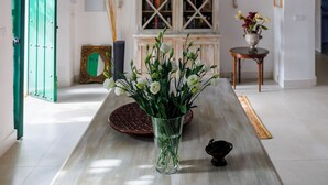 A room with a wooden ceiling, a chandelier, a table with a vase of flowers, and a cabinet with glass doors.
