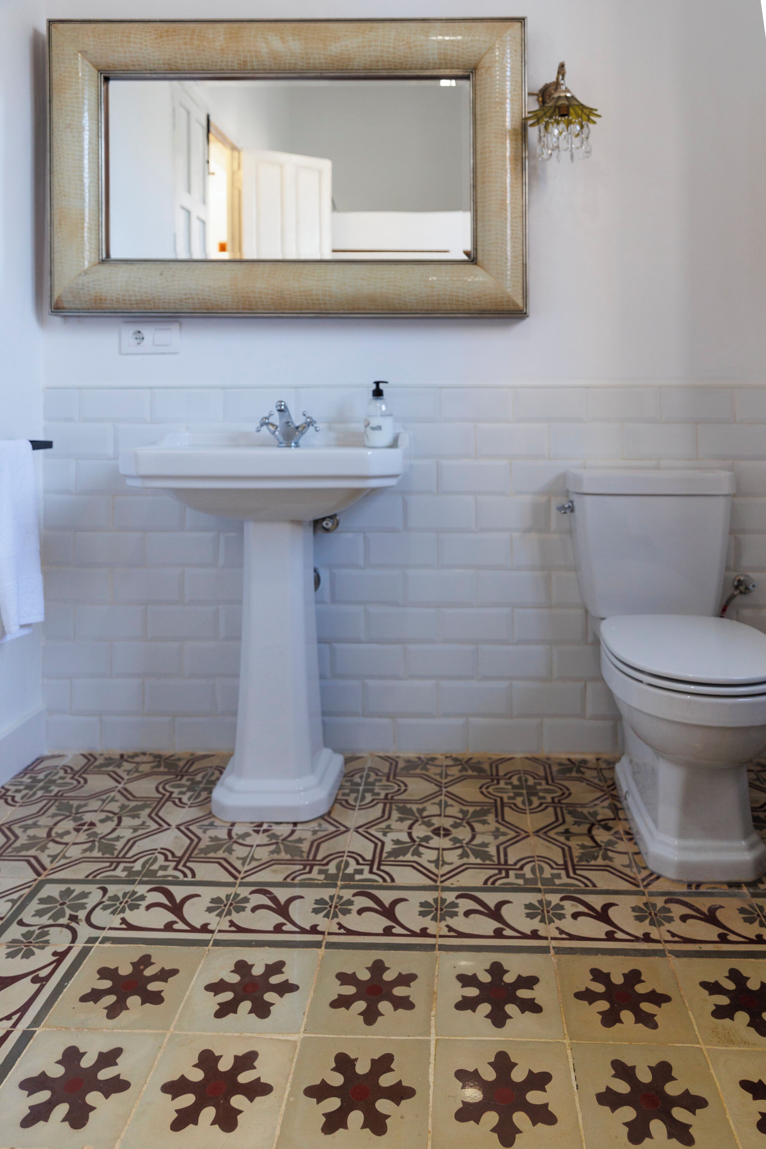 A bathroom with a white sink, toilet, and a mirror above the sink. The floor has patterned tiles.