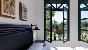 A room with a bed, a nightstand, a wall-mounted lamp, and two windows with green frames.