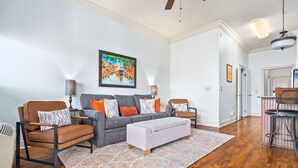 Una sala moderna con un sofá gris, sillones marrones, un otoman blanco y una alfombra estampada.