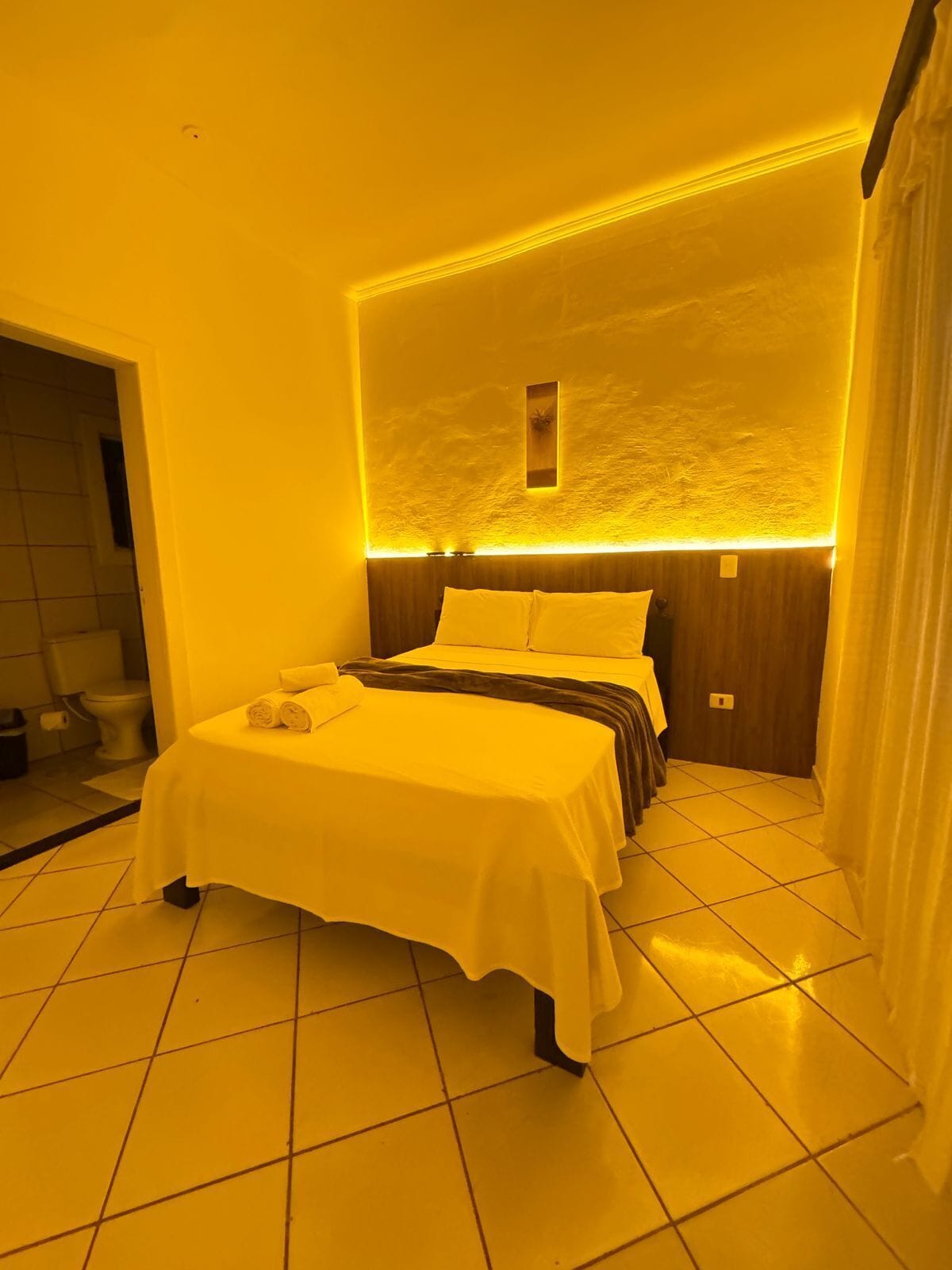 Una habitación de hotel con una cama, una mesita y un baño visible a través de una puerta abierta.