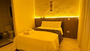 Una habitación de hotel con una cama, una mesita y un baño visible a través de una puerta abierta.
