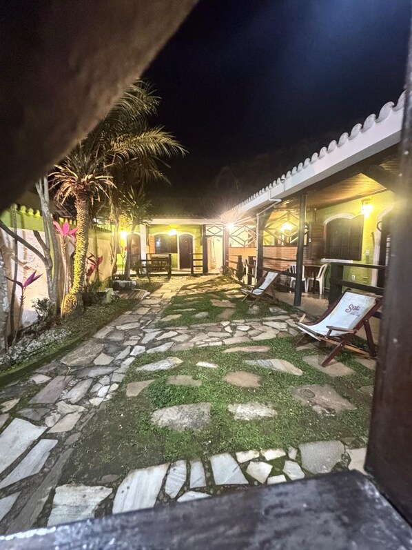 A courtyard with stone paving, a palm tree, and a covered seating area with chairs. - Pousada Barra Do Sahy (São Sebastião)