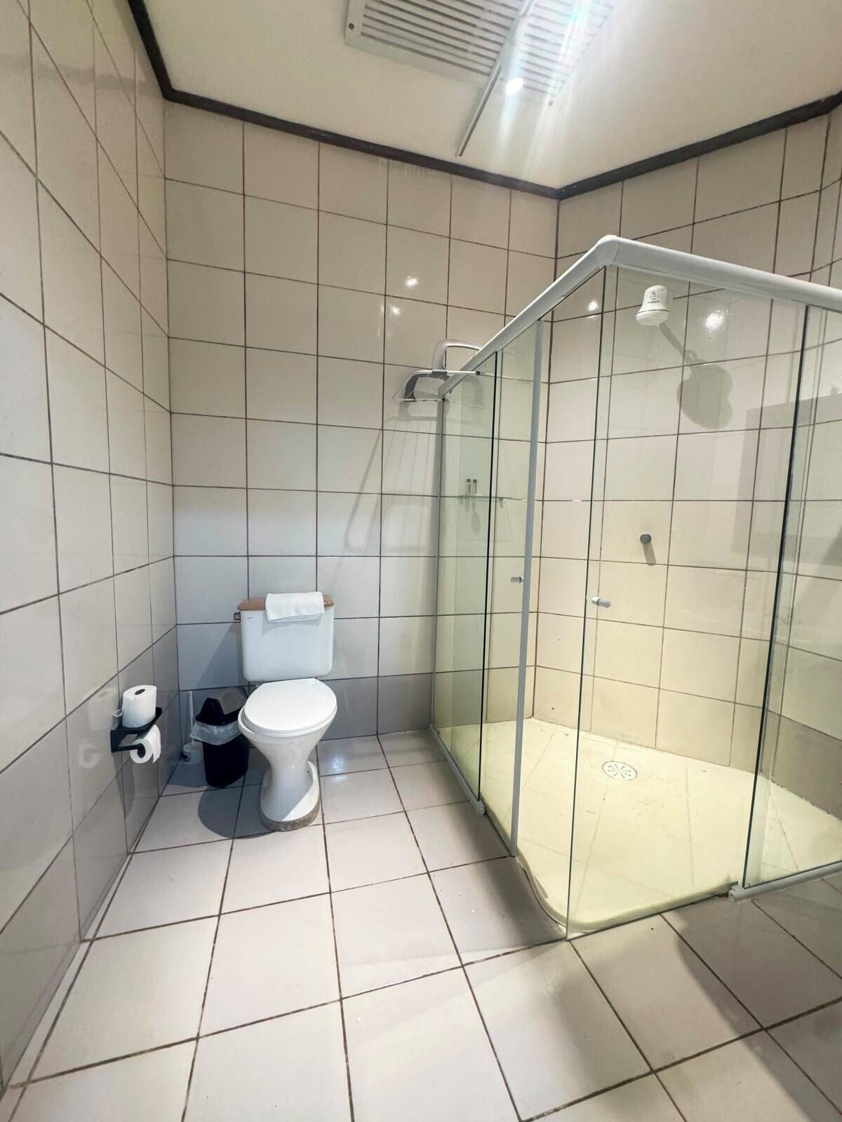 Un baño moderno con ducha envuelta en vidrio, inodoro y cubo de basura.