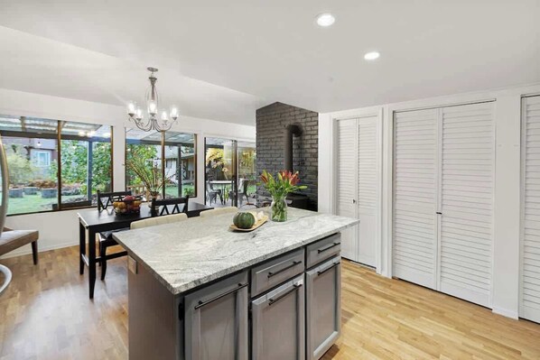 A modern kitchen with a marble island, built-in cabinets, and a black brick fireplace.