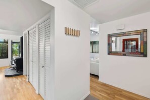 A hallway with a wooden floor, white walls, a door with white shutters, and a mirror with a decorative frame.