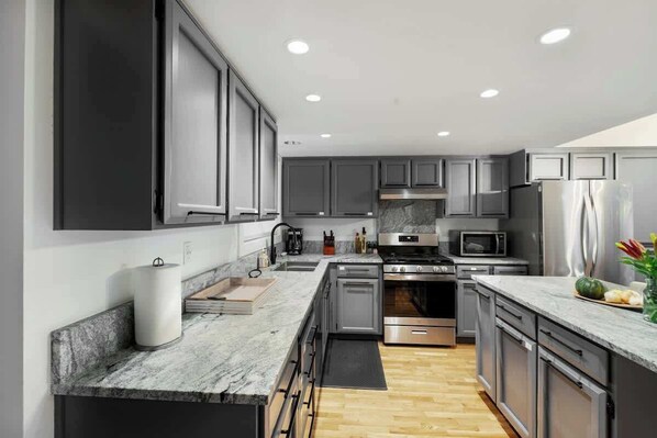 A modern kitchen with grey cabinets, stainless steel appliances, and a marble countertop.