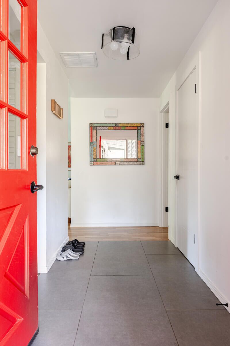 A hallway with a red door, a mirror, and a pair of shoes on the floor.