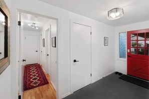 A hallway with white walls, a red door, and a patterned rug leading to a door.