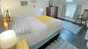 Une chambre à coucher avec un lit, une commode, une chaise et des œuvres d’art accrochées aux murs.