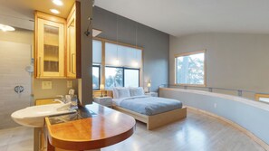 A modern bedroom with a bed, bedside tables, a window, and a bathroom with a sink and mirror. - Deck Views, Fire Pit, Pool, 3 Mins to Beach Madrona Tree Retreat by Avantstay (Coupeville)