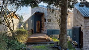 Une maison moderne avec une façade en bois, un porche à l’avant et un petit jardin.