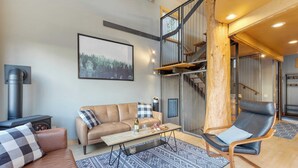 A modern living room with a sofa, a coffee table, a chair, a fireplace, and a staircase. - Deck Views, Fire Pit, Pool, 3 Mins to Beach Madrona Tree Retreat by Avantstay (Coupeville)
