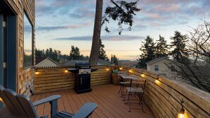A wooden deck with a barbecue grill, outdoor seating, and a view of the surrounding landscape. - Deck Views, Fire Pit, Pool, 3 Mins to Beach Madrona Tree Retreat by Avantstay (Coupeville)